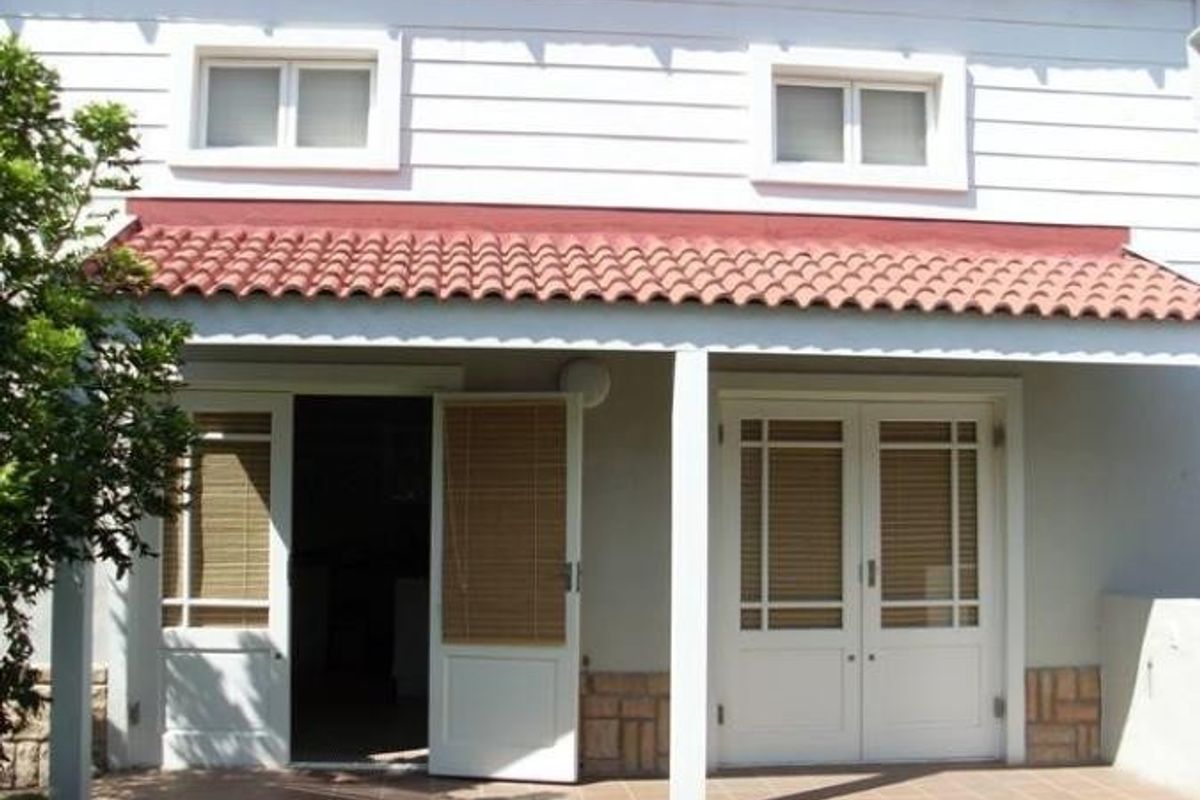 A covered rear patio featuring tiled flooring, stone base detailing, and multiple glass-paneled doors providing access to the interior.