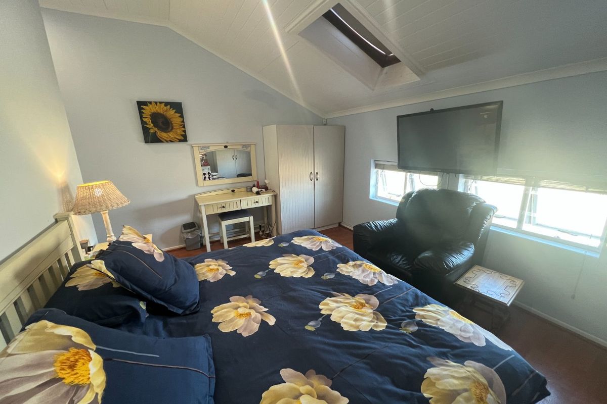 A cozy bedroom featuring a vaulted ceiling with a skylight, laminate flooring, and built-in wardrobe storage.