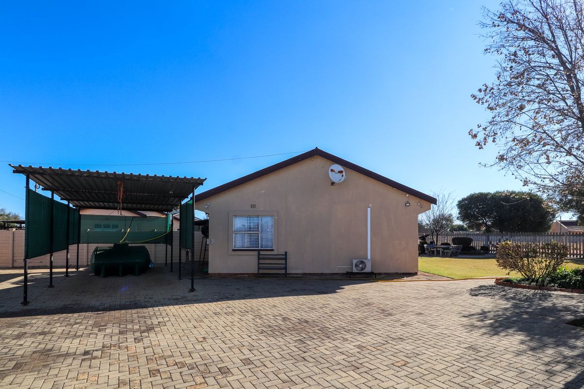 Rear view of the property featuring a paved driveway, a covered carport, and a well-maintained garden area.