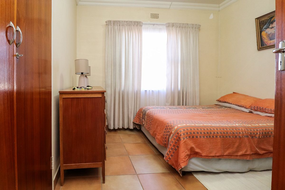 A functional bedroom featuring tiled flooring, a built-in wardrobe, and a window with curtains, offering a neutral base for potential interior updates.
