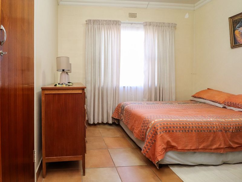 A functional bedroom featuring tiled flooring, a built-in wardrobe, and a window with curtains, offering a neutral base for potential interior updates.
