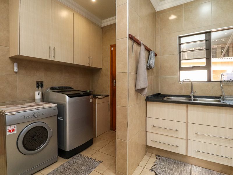 A functional laundry room featuring built-in cabinetry, a stainless steel sink, tiled walls, and dedicated space for laundry appliances.