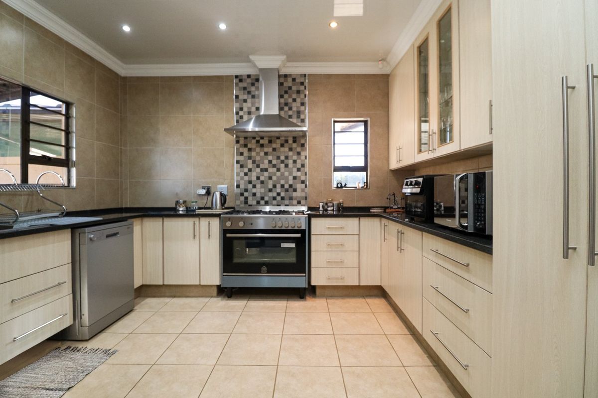 A well-maintained kitchen featuring light wood cabinetry, granite countertops, a stainless steel oven with extractor fan, and neutral tiled finishes.