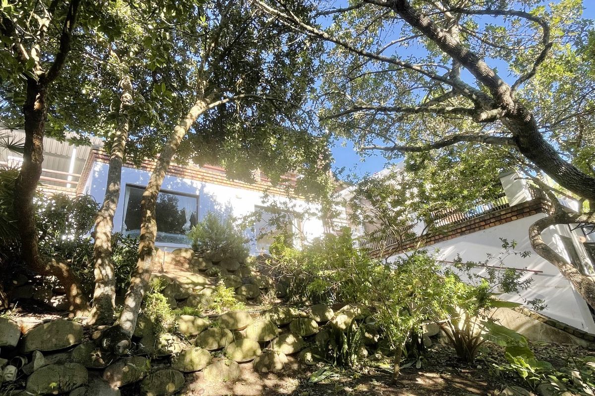 A view of the rear elevation featuring a stone retaining wall, landscaped garden area, and an elevated terrace with a brick balustrade.