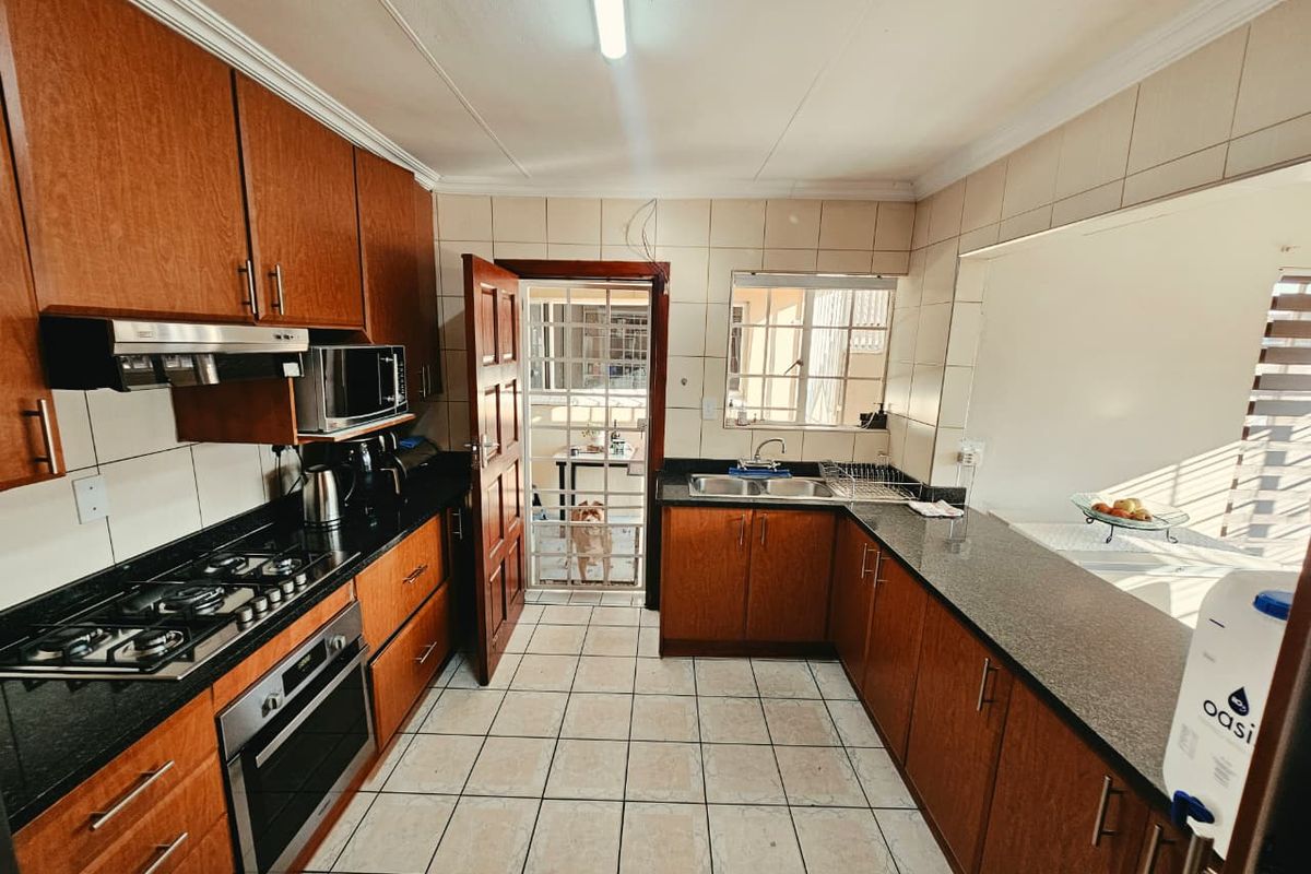 A functional kitchen featuring wooden cabinetry, granite countertops, a gas hob, built-in oven, and tiled finishes with direct access to an outdoor area.