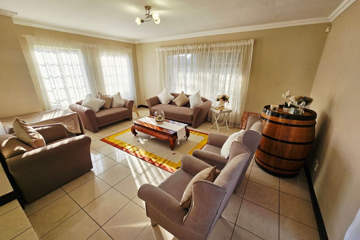 A spacious living room featuring neutral tiled flooring, large windows with sheer curtains, and classic ceiling cornicing, providing a bright and comfortable seating area.