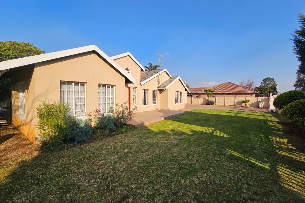 A well-maintained rear exterior view of the house featuring a paved patio area, a spacious lawn, and a secure boundary wall.