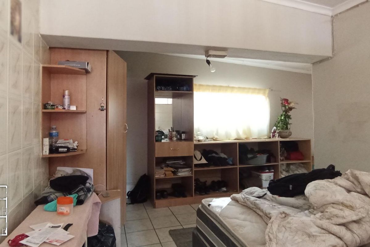 A bedroom featuring tiled flooring, built-in storage units, and a wardrobe, requiring cosmetic updates to the wall finishes and lighting fixtures.