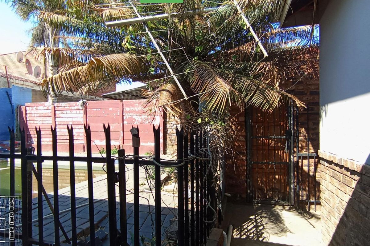 Rear exterior area featuring a paved walkway, brick boundary wall, and metal security gate, with visible signs of wear and maintenance requirements.