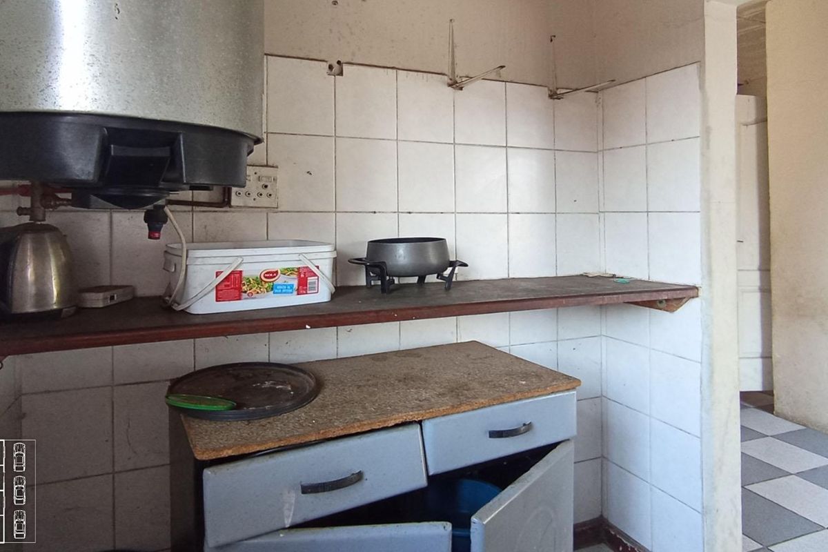 A dated kitchen area featuring basic base cabinetry, tiled splashbacks, and a wall-mounted electric water heater, requiring significant renovation and modernization.