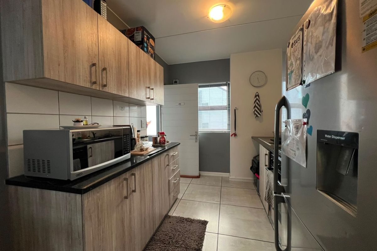A functional kitchen featuring wood-look cabinetry, dark countertops, tiled backsplash, and neutral floor tiles, providing a clean and practical workspace.