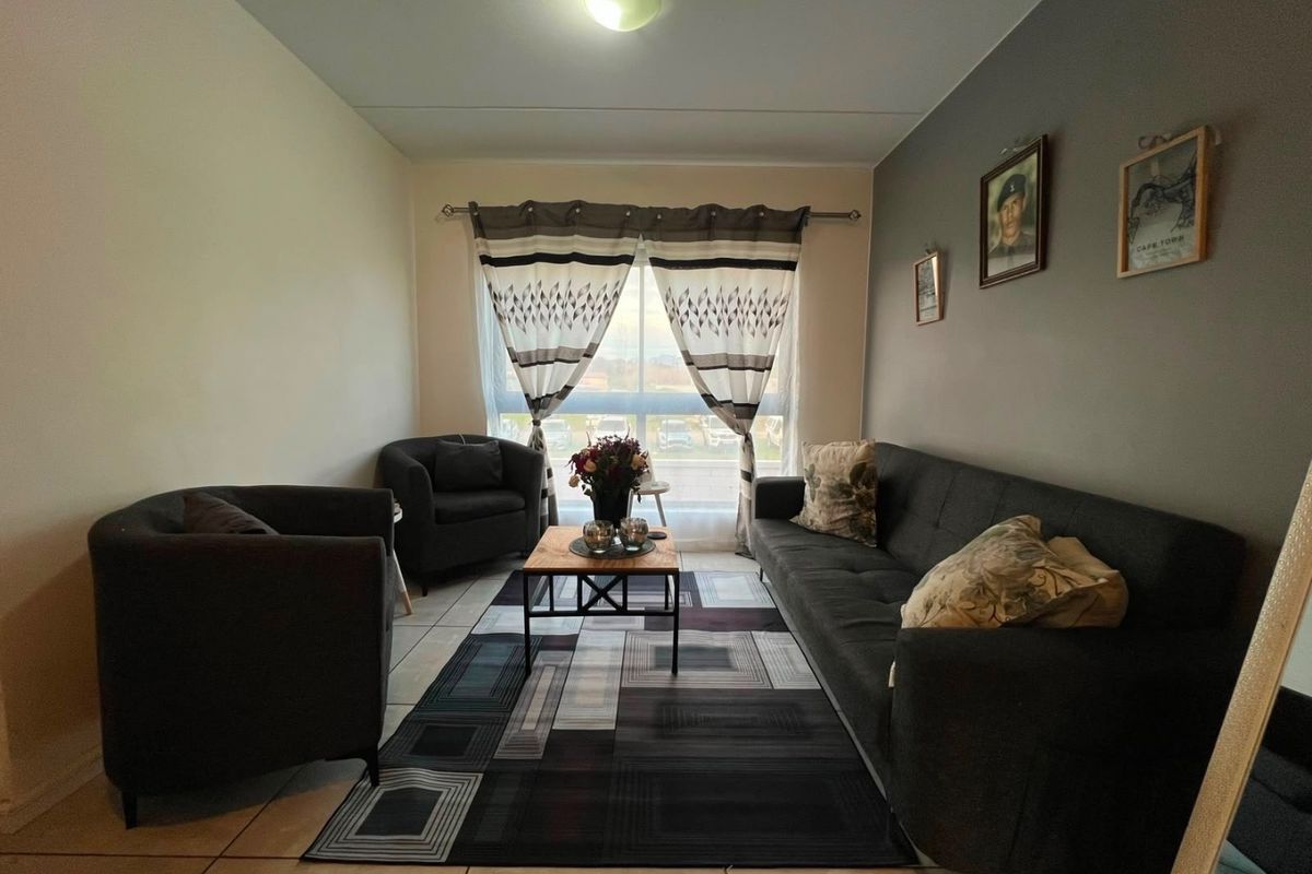 A comfortable living room featuring tiled flooring and a large window with curtain rod, providing natural light to the space.