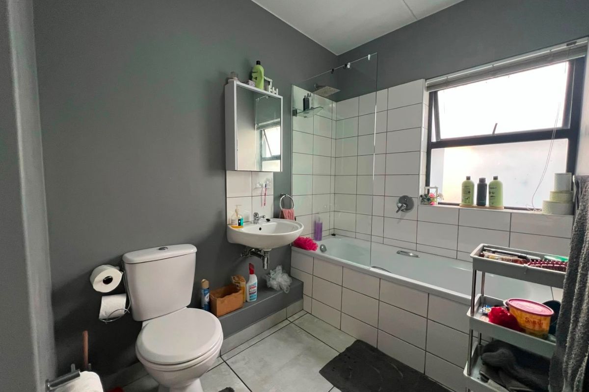 A functional bathroom featuring a bathtub with a glass shower screen, wall-mounted basin, and tiled finishes, providing a practical space for daily use.