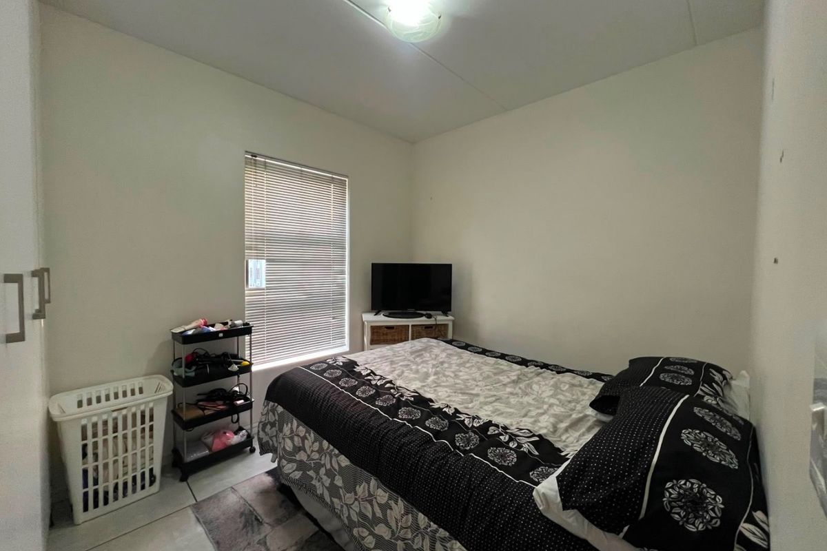 A functional bedroom featuring a built-in wardrobe, tiled flooring, and a window fitted with venetian blinds.