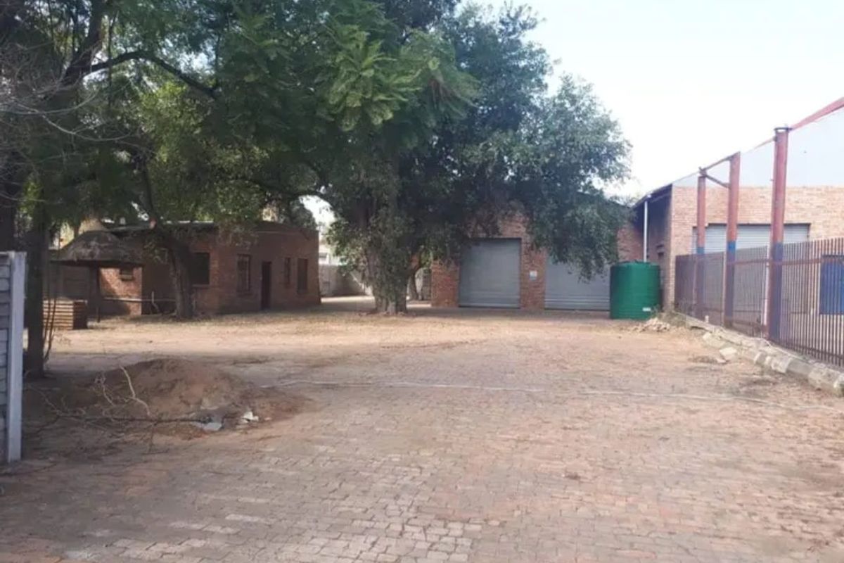 Spacious commercial yard area featuring brick paving, multiple roller shutter doors, and secure steel palisade fencing, suitable for industrial or storage use.