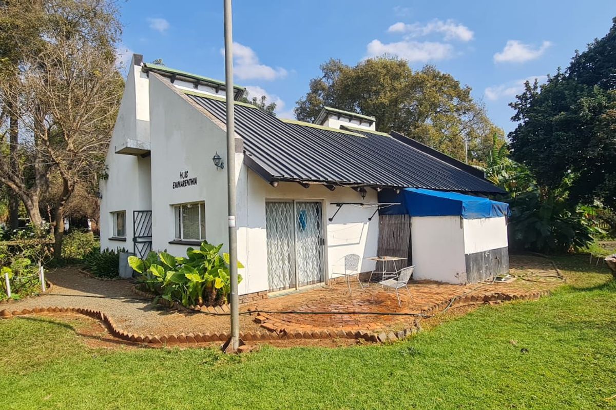 Rear view of a farm cottage featuring a metal roof, brick patio area, and established garden surroundings.