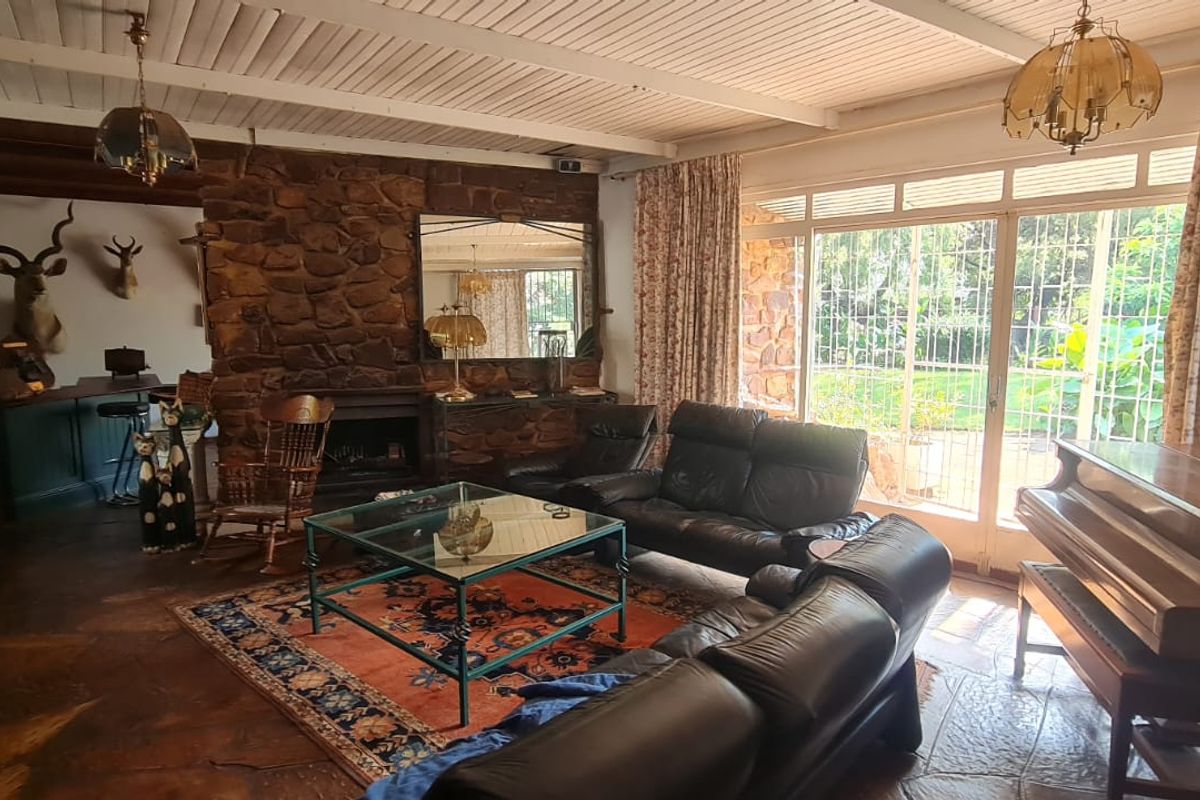 Spacious living room featuring a rustic stone fireplace, exposed beam ceiling, flagstone flooring, and large sliding glass doors opening to the garden.