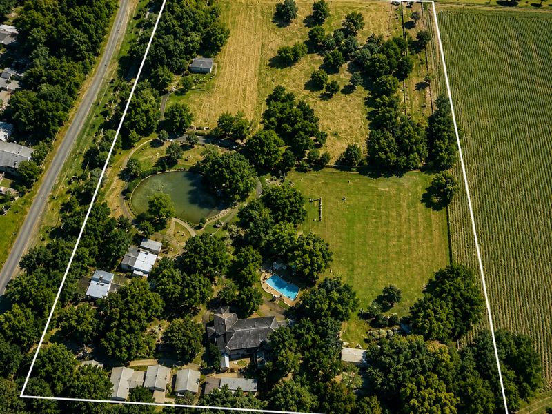 Aerial view of a large farm property featuring a main residence, swimming pool, private pond, mature trees, and extensive open pasture land.