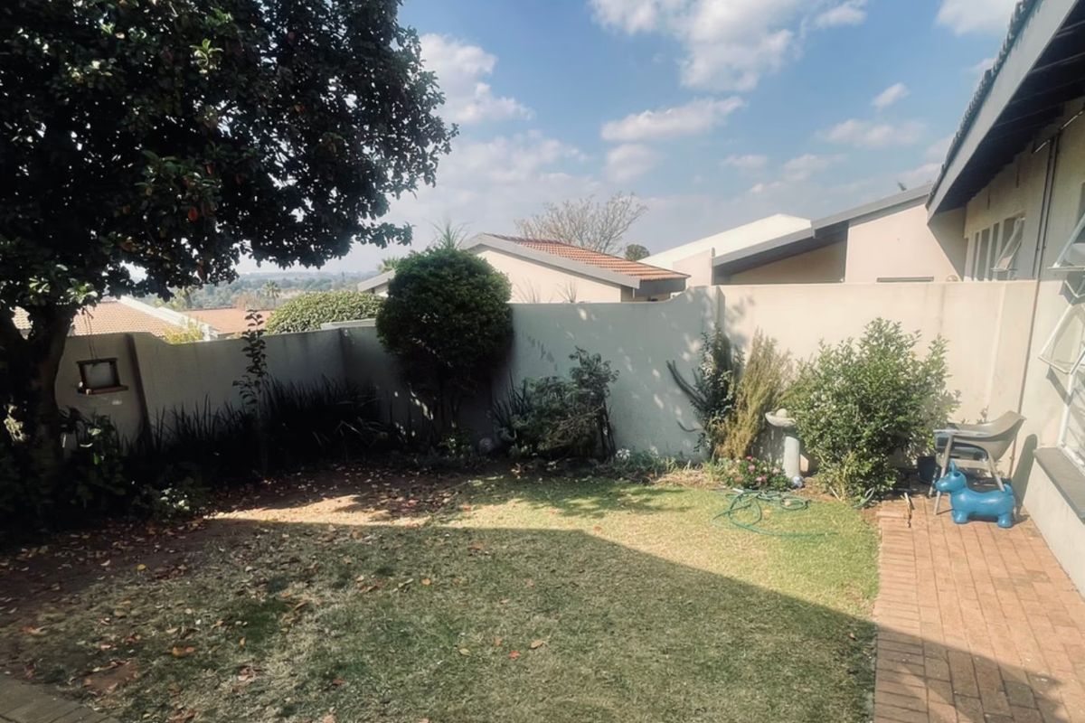 A private rear garden featuring a lawn area, perimeter boundary walls, and brick paved pathway adjacent to the townhouse structure.