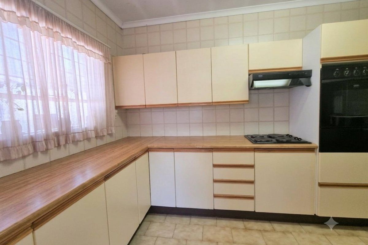A functional kitchen featuring laminate countertops, built-in cabinetry, a gas hob, extractor fan, and a built-in oven with tiled finishes.