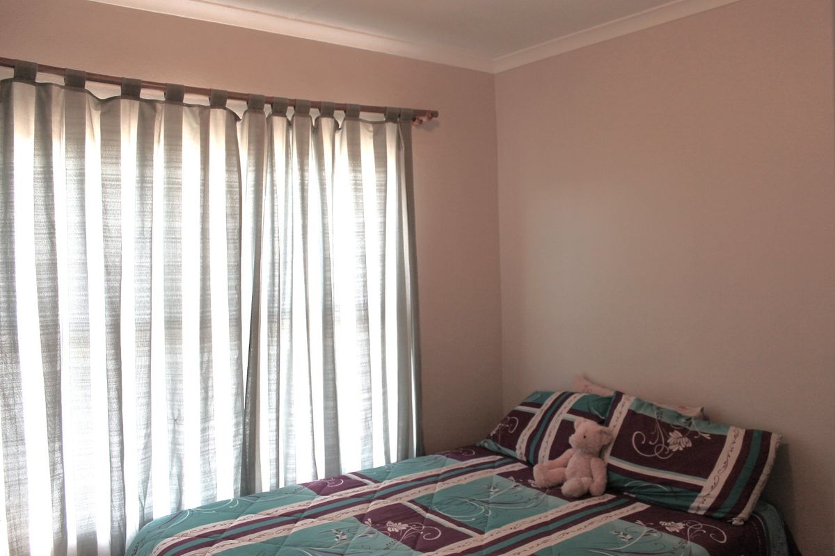 A simple bedroom featuring neutral wall tones and a window fitted with a curtain rod.