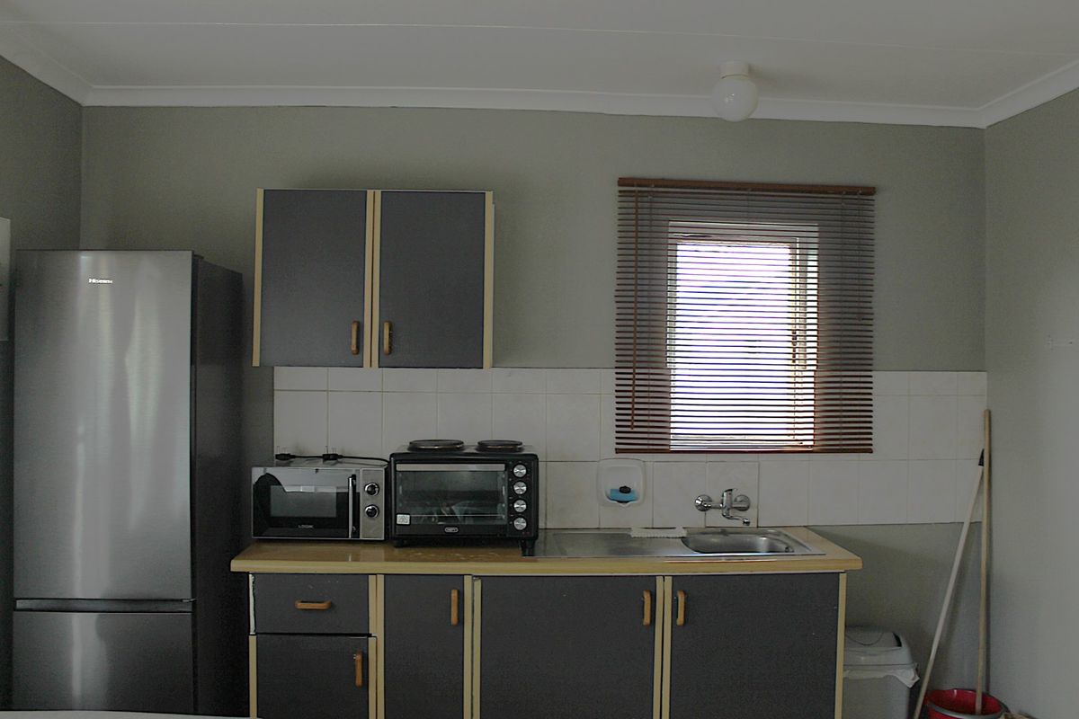 A functional kitchen area featuring grey cabinetry, a stainless steel sink, tiled backsplash, and a window with venetian blinds.