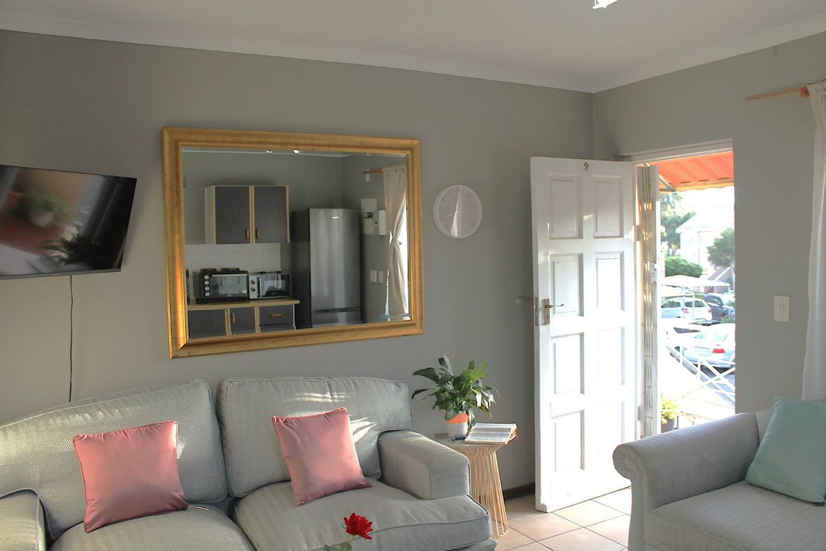 A living room area featuring tiled flooring and a panelled entrance door, with a view into the adjacent kitchen area.
