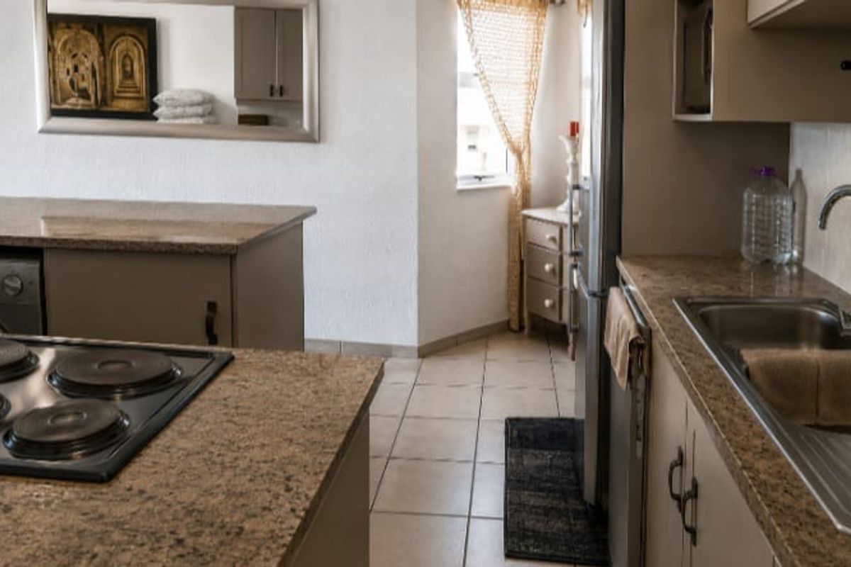A functional kitchen featuring granite countertops, an integrated electric hob, stainless steel sink, and tiled flooring with ample built-in cabinetry.