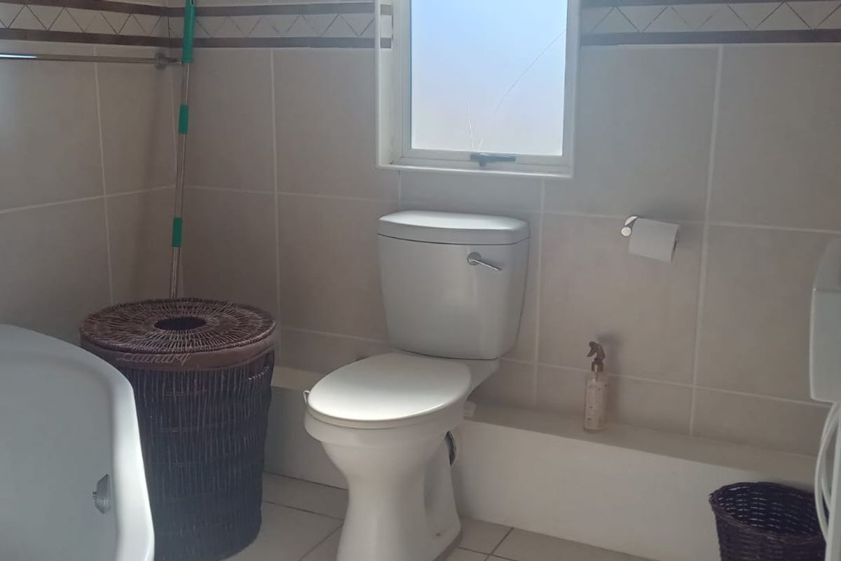 A functional bathroom featuring tiled walls and flooring, a standard toilet, a bathtub, and a vanity basin with a window.