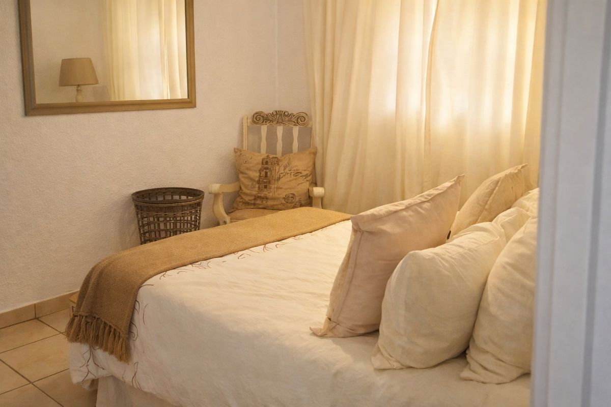 A cozy bedroom featuring neutral tones, tiled flooring, and a wall-mounted mirror, creating a warm and inviting atmosphere.