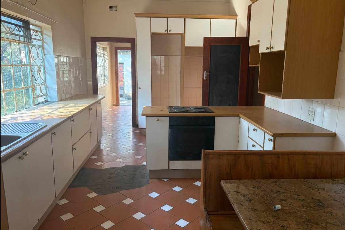 A dated kitchen featuring built-in cabinetry, laminate countertops, an integrated oven and hob, and tiled flooring, offering significant potential for modernization.