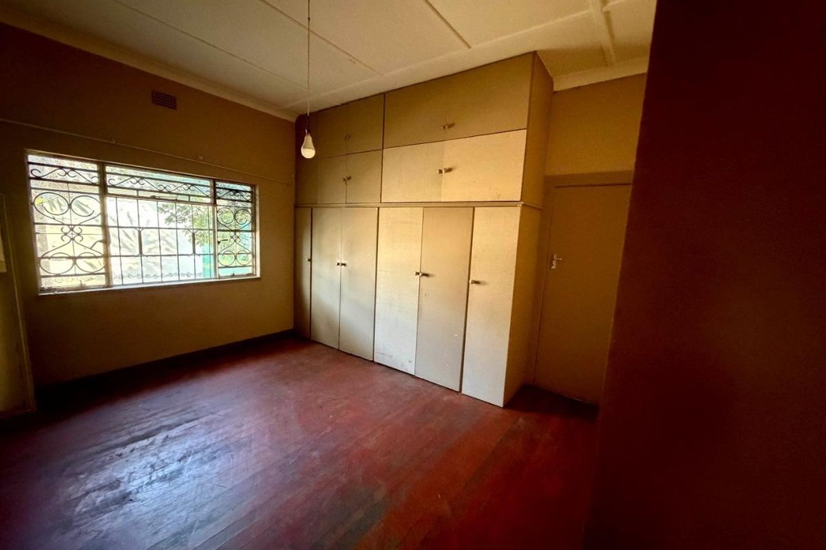 An empty bedroom featuring original timber flooring, built-in floor-to-ceiling cupboards, and security bars on the window.