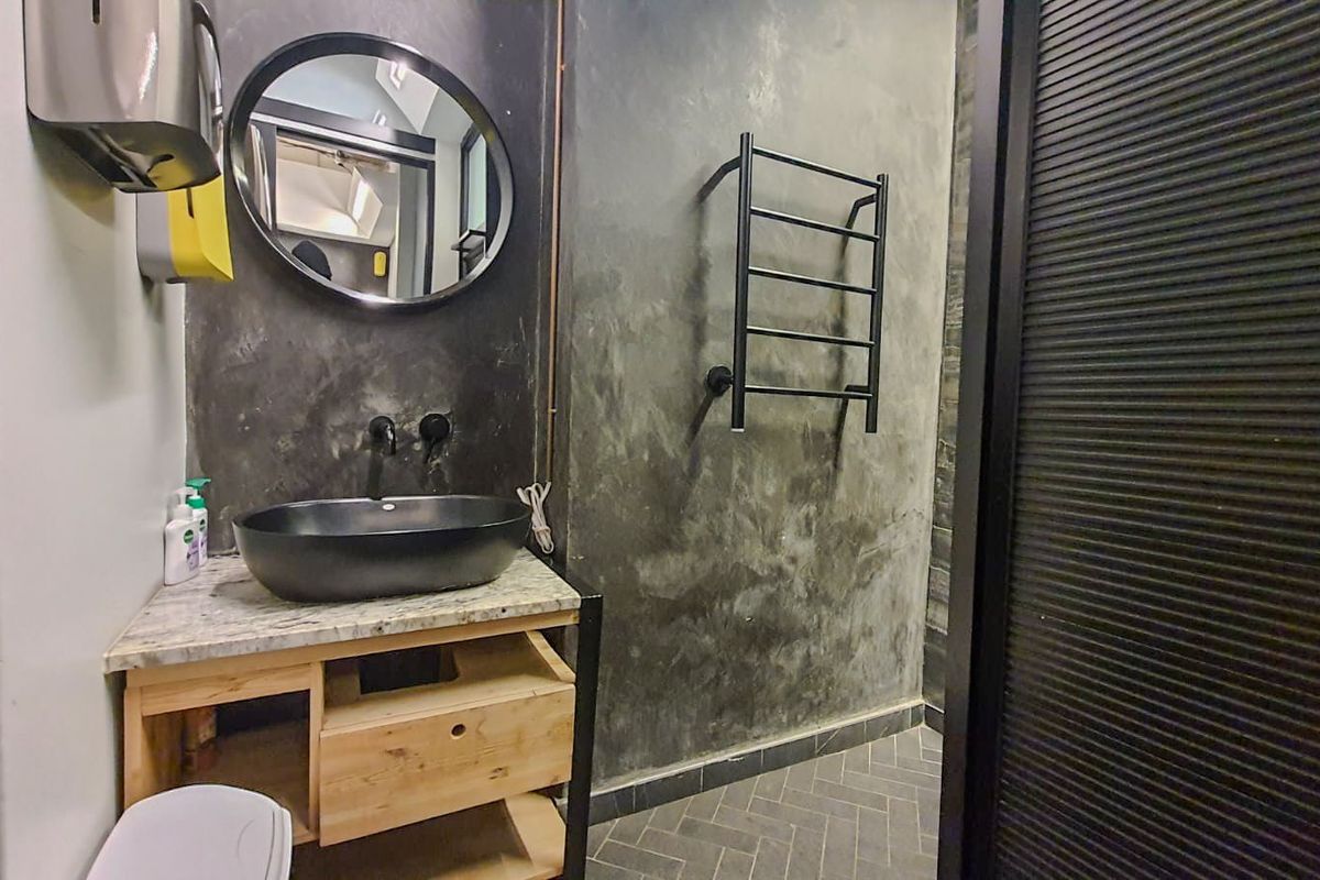 Modern industrial-style bathroom featuring a vessel sink, stone vanity top, heated towel rail, and distinctive herringbone floor tiling with concrete-effect walls.