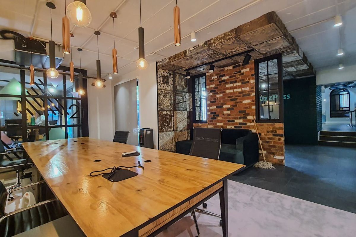Modern commercial office space featuring industrial design elements, exposed brickwork, stylish pendant lighting, and glass-partitioned meeting areas.