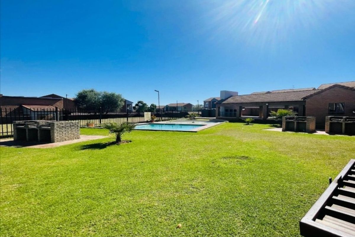 Communal outdoor area featuring a swimming pool, landscaped lawn, and brick built-in braai facilities within a secure residential complex.