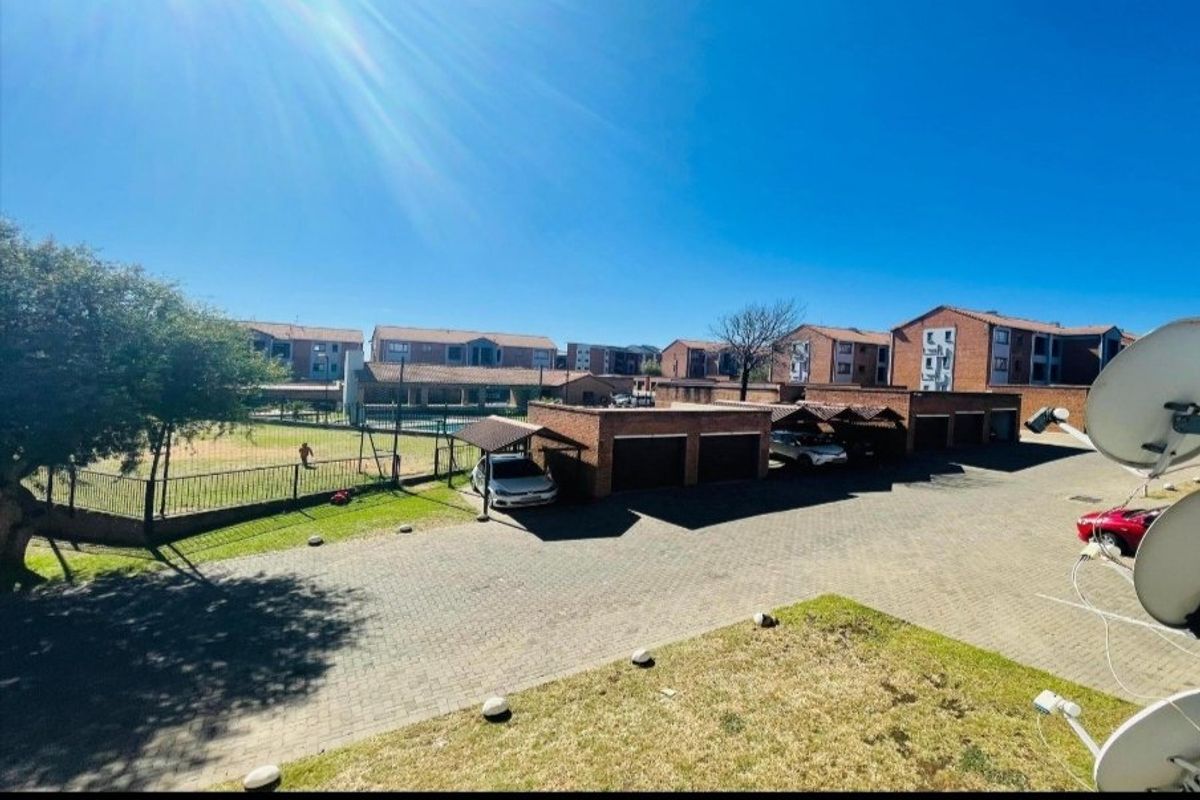 An elevated view of the apartment complex grounds, featuring a paved driveway, row of brick garages, and communal lawn area.