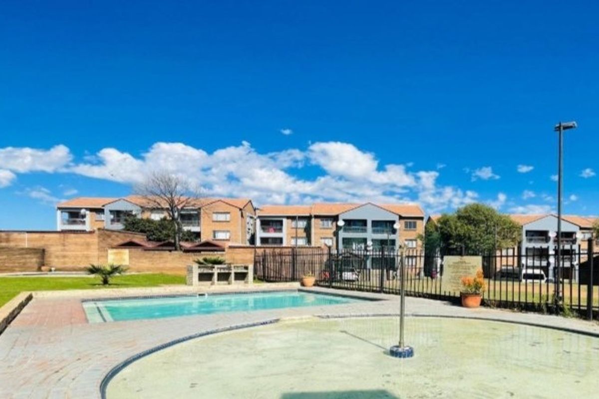 Communal outdoor area featuring a swimming pool, wading pool, and built-in braai facilities within a fenced complex setting.