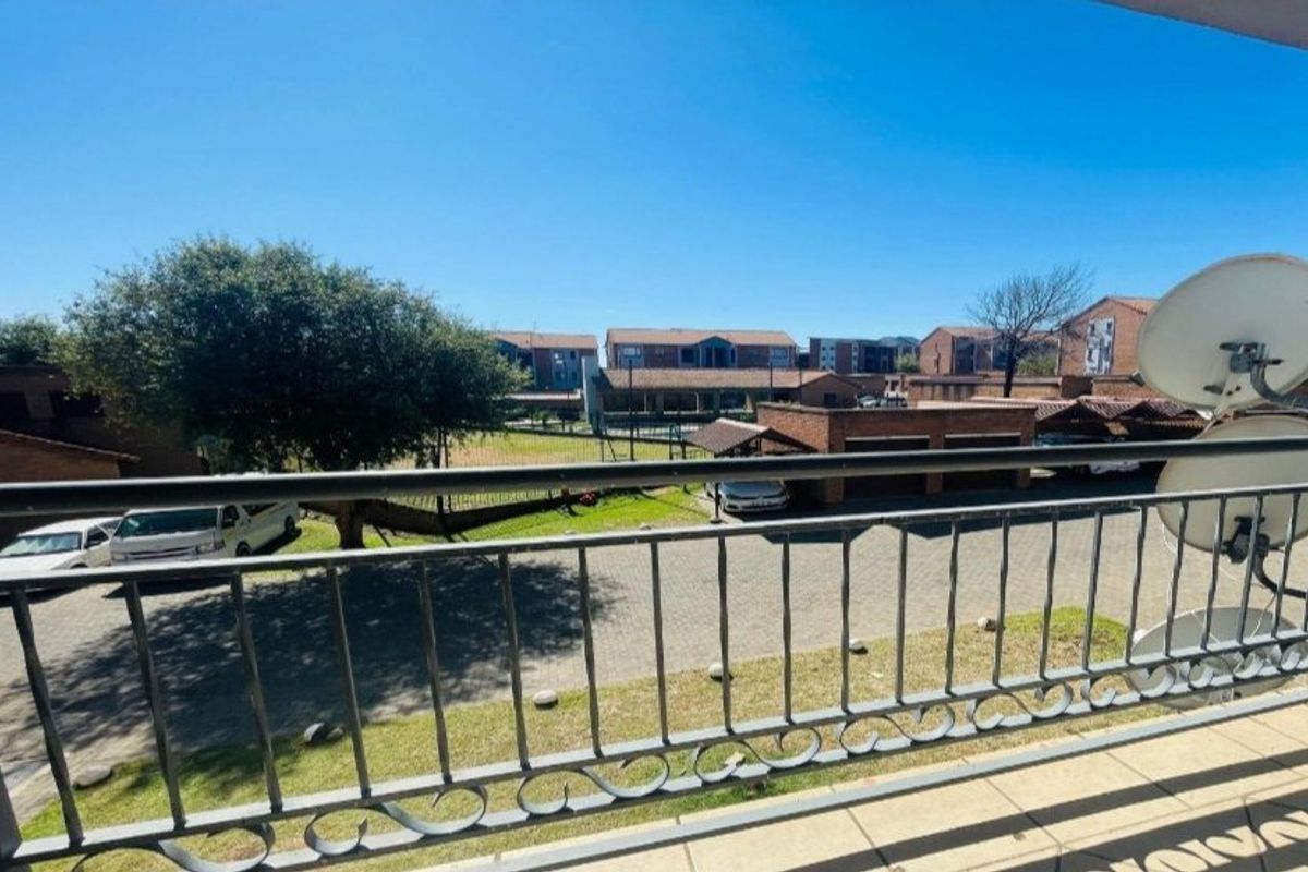 A balcony with a metal balustrade overlooking the apartment complex grounds and parking area.