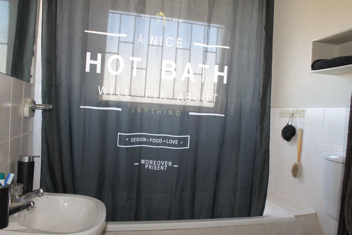 A functional bathroom featuring a bathtub with a shower curtain, a basin, and tiled wall finishes with a built-in storage shelf.
