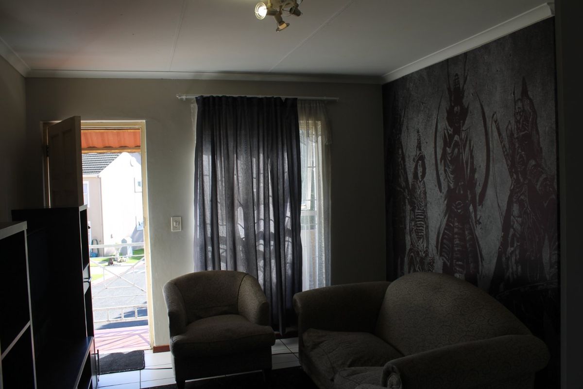 A living room area featuring tiled flooring, a ceiling light fixture, and direct access to an exterior space through a doorway.