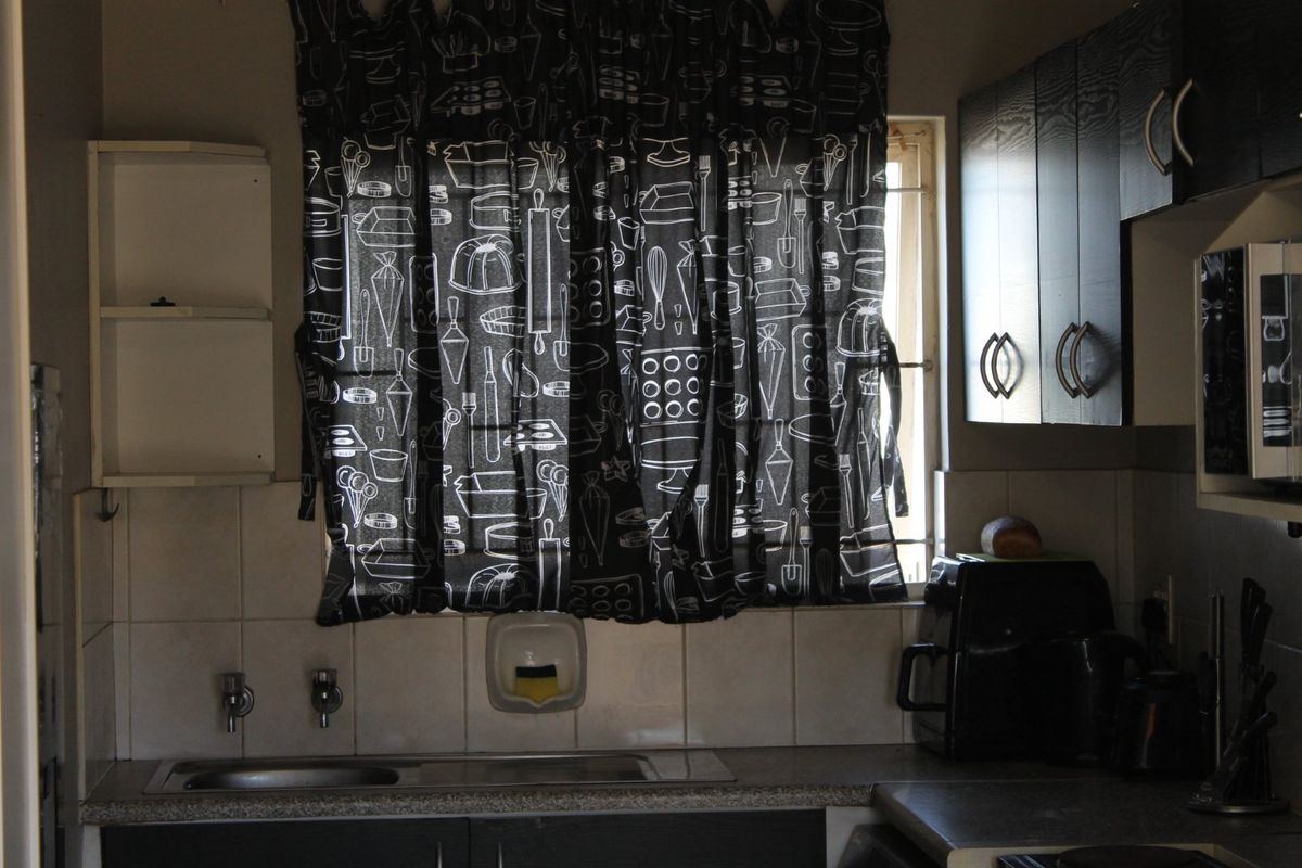 A functional kitchen area featuring built-in dark cabinetry, a stainless steel sink, tiled backsplash, and a window with security bars.
