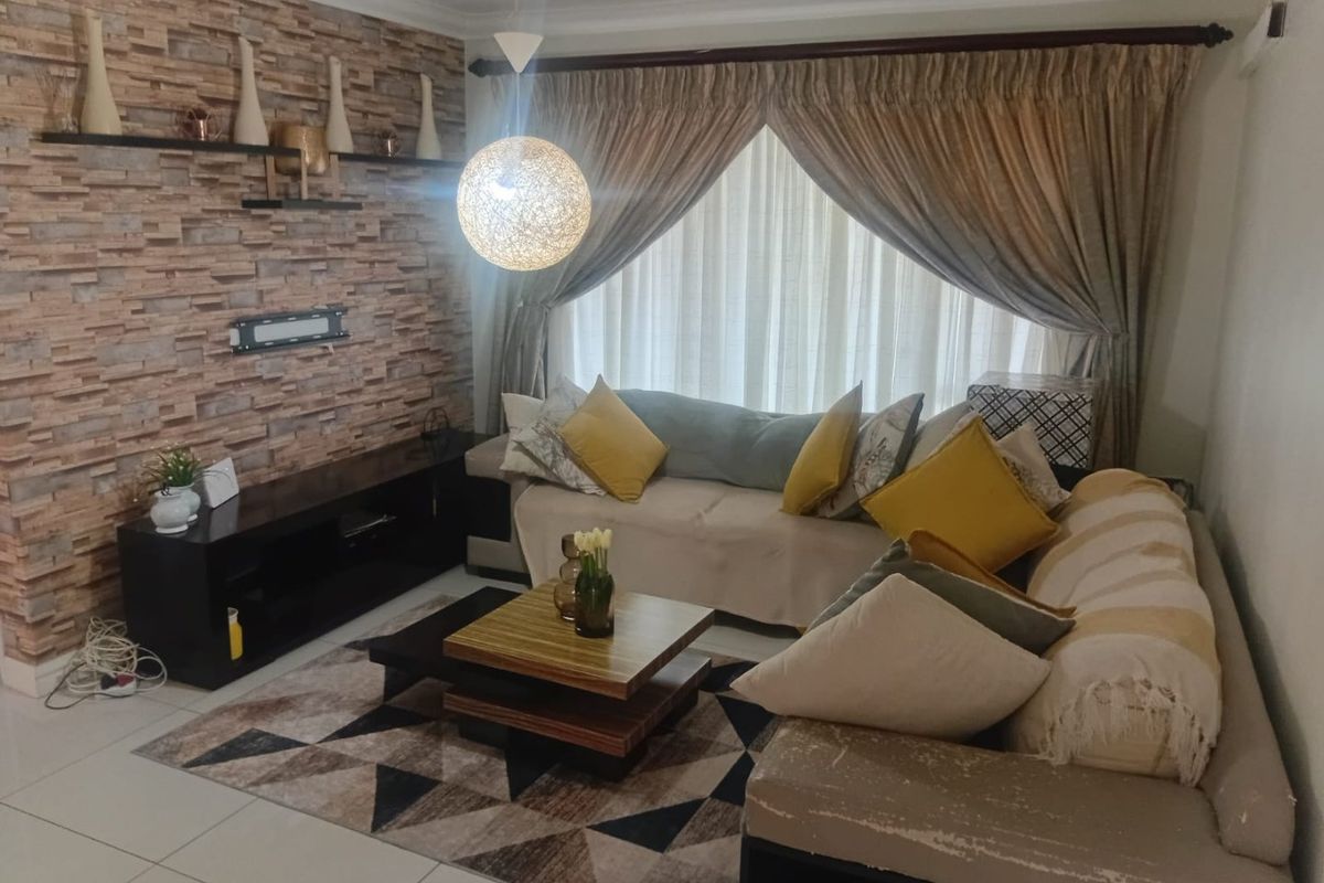 A cozy living room featuring a textured stone-cladding accent wall, tiled flooring, and a central pendant light fixture.