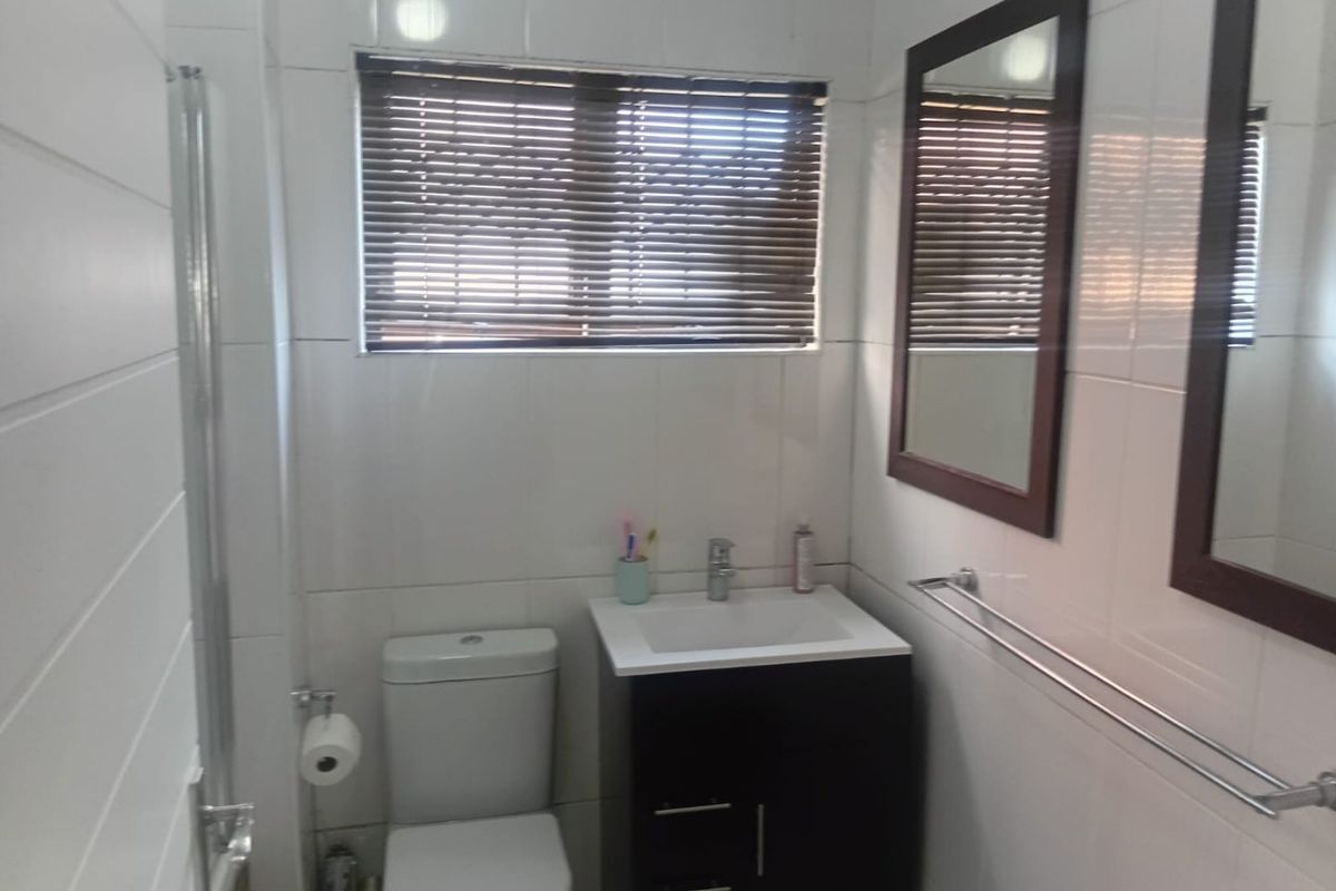 A compact bathroom featuring a modern vanity cabinet, white basin, toilet, and wall-mounted mirror with tiled finishes.