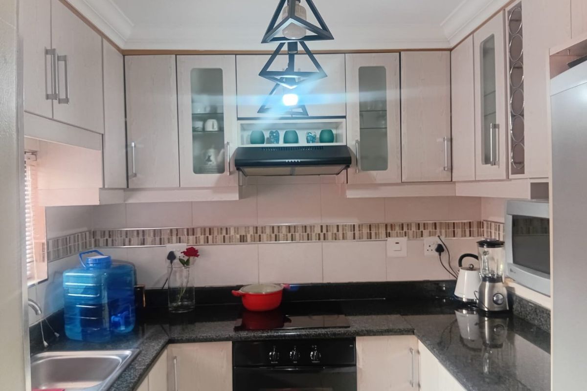 A functional kitchen featuring granite countertops, built-in oven with hob, extractor fan, and ample cabinetry with glass-fronted display sections.