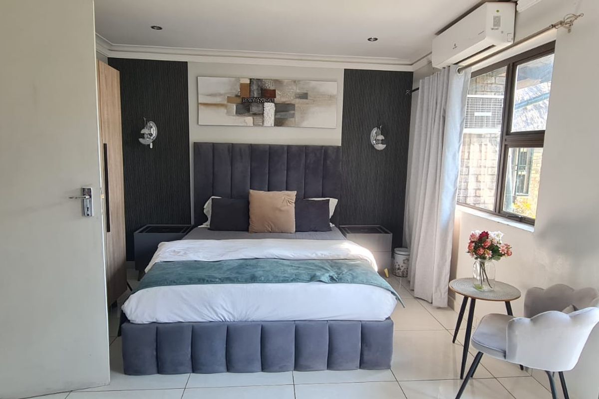 A well-maintained bedroom featuring tiled flooring, recessed downlighting, and a wall-mounted air conditioning unit.