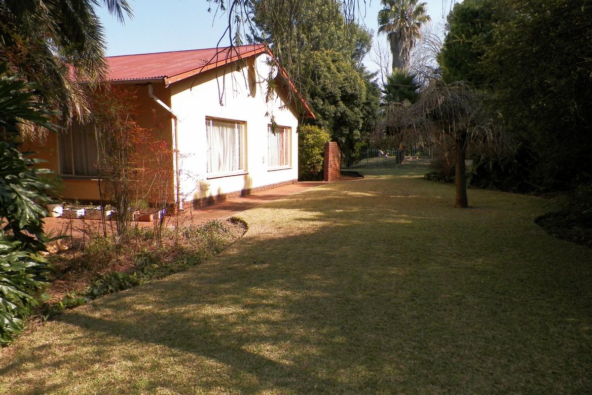 A view of the rear elevation of the house featuring a corrugated metal roof, brick patio, and a well-maintained garden area.