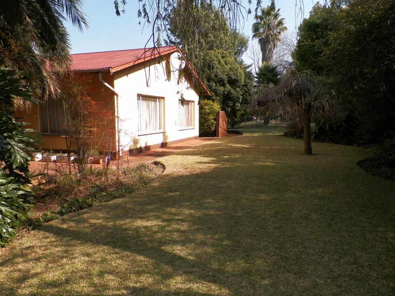 A view of the rear elevation of the house featuring a corrugated metal roof, brick patio, and a well-maintained garden area.