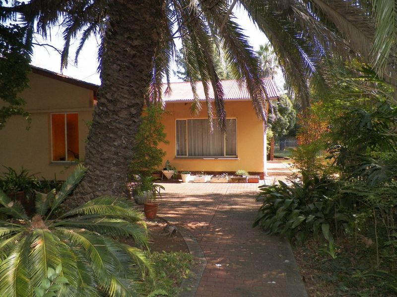 A view of the rear exterior of the house featuring brick paving, mature landscaping, and a metal roof.