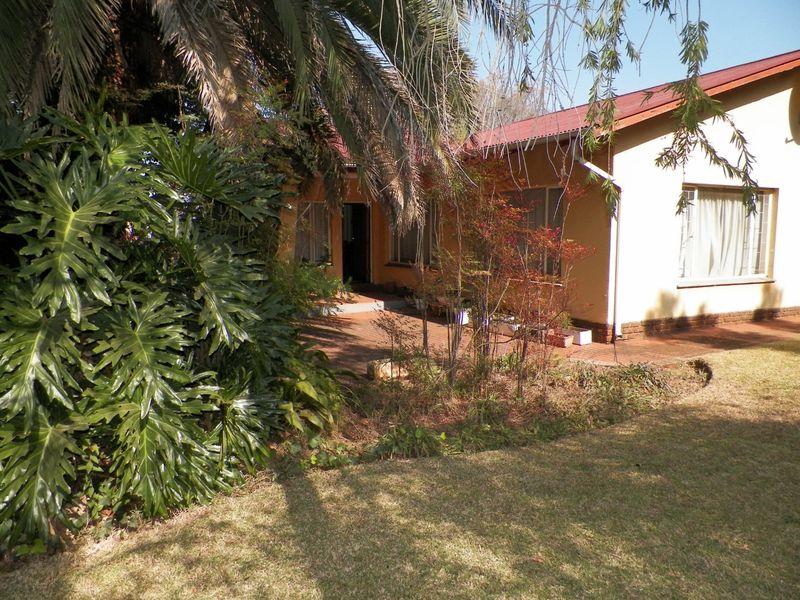 Rear view of the house featuring a brick paved patio area, metal roofing, and established garden landscaping.