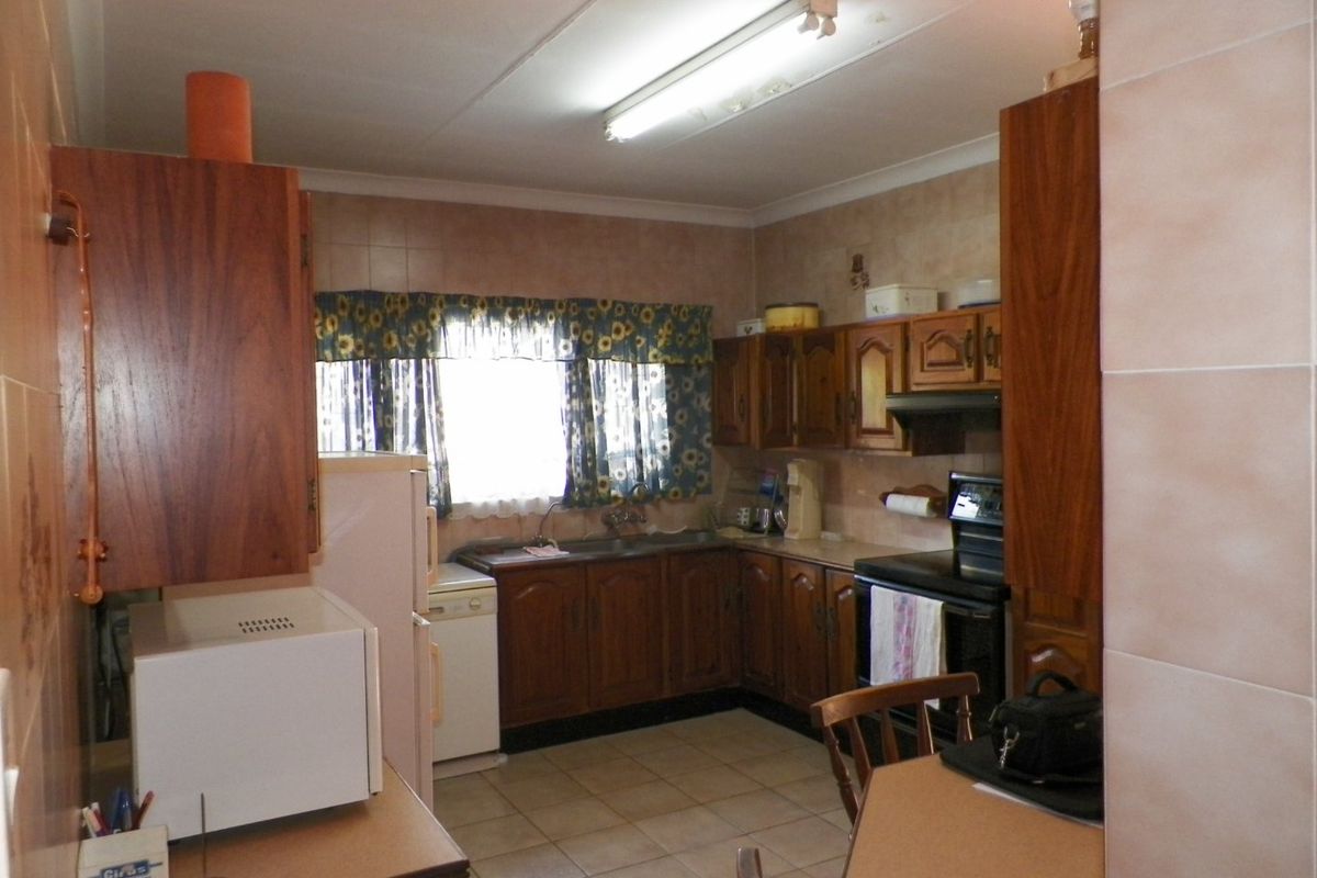 A dated kitchen featuring wooden cabinetry, tiled flooring, and a functional layout with a double basin sink and built-in stove area.